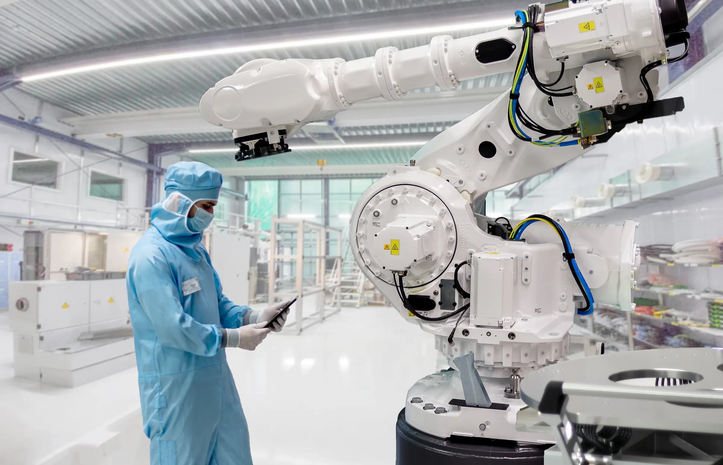 Un tecnico in tuta da camera bianca consulta un tablet accanto a un grande robot industriale a sei assi
